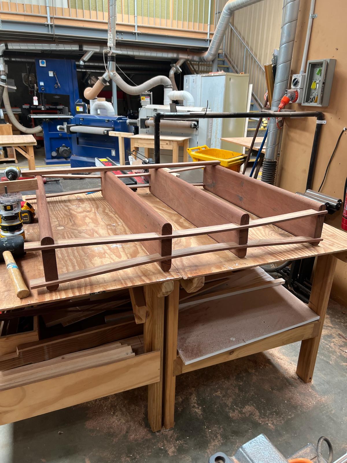 Jarrah strips bent to a gentle bow to form the sides of a four-tier shelf frame, laid on a workshop bench