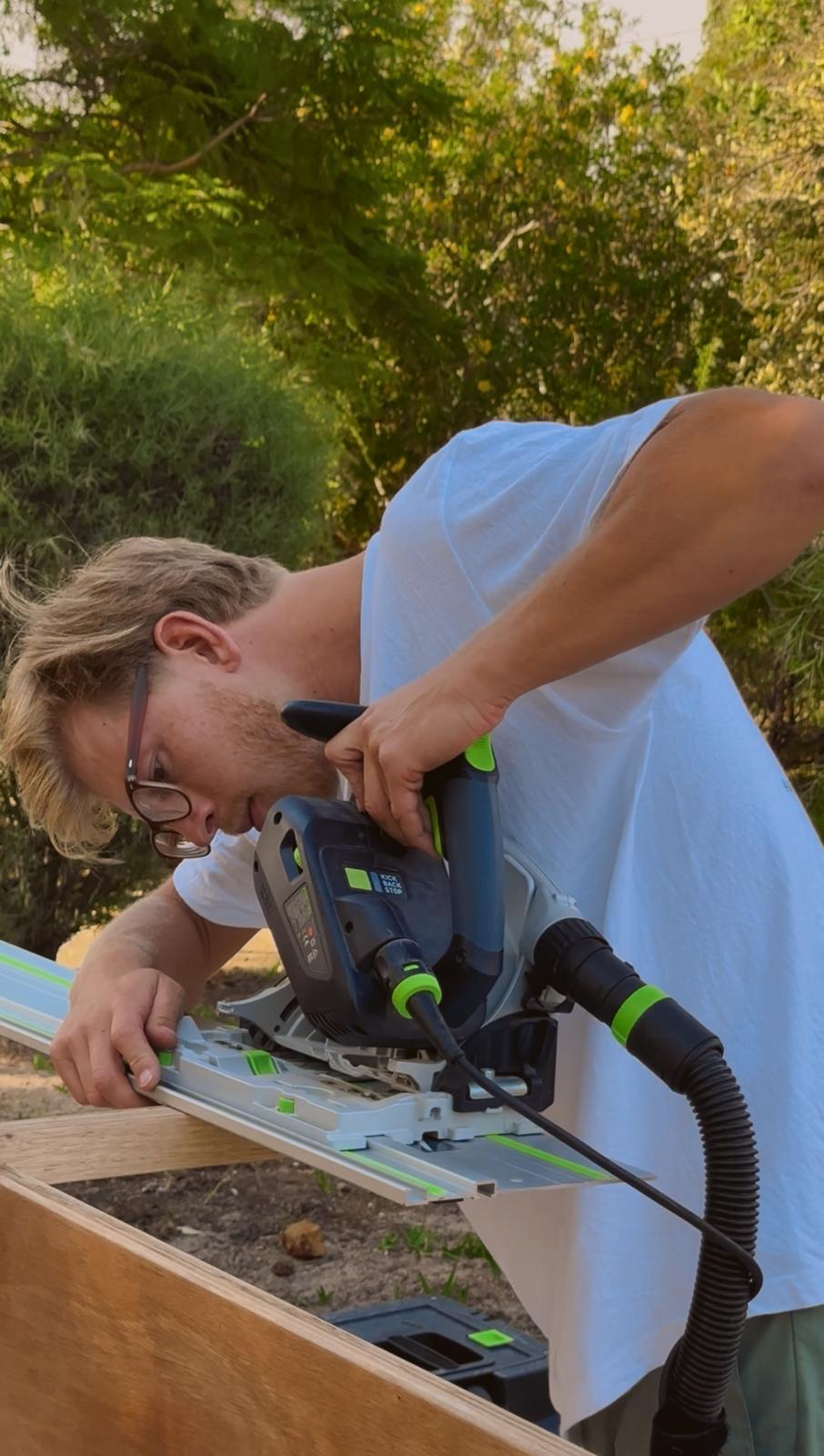 Track saw on a guide rail cutting a plywood panel with dust extraction attached