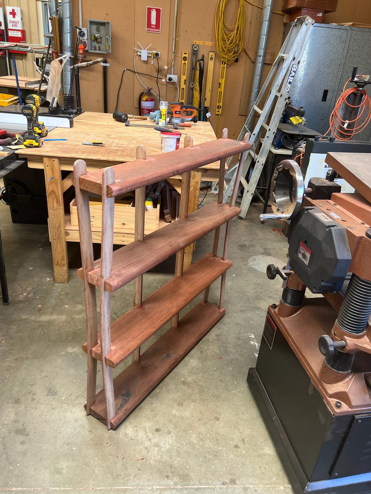 Assembled jarrah shelf frame standing in the workshop, the bent strips bowing out towards the base